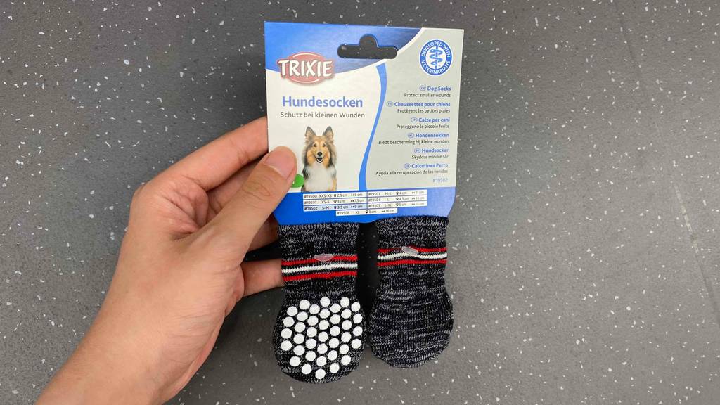 Hand hält graue getestete Trixie-Hundesocken in der Verpackung.