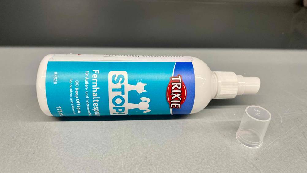Eine offene Flasche getestetes Katzen-Fernhaltespray liegt quer auf einer weißen Fläche, daneben die Verschlusskappe.
