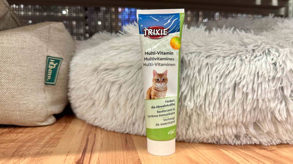 Eine Tube Vitamine für Katzen steht zum testen vor einem weißen Flauschkissen.
