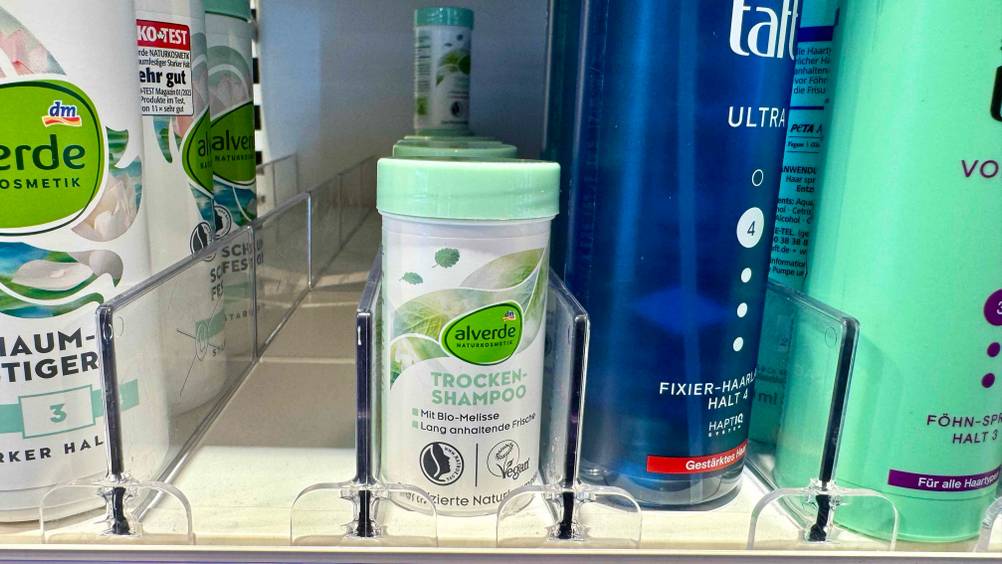 Mehrere getestete Trockenshampoo-Puder in einem Verkaufsregal neben anderen Produkten.