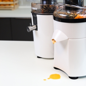 2 Entsafter stehen nebeneinander auf einem Tisch, ein Entsafter hat Saft auf den Tisch tropfen lassen.