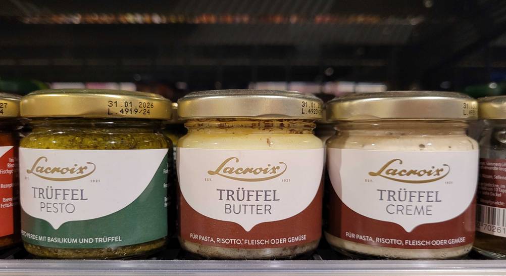 In einem Regal stehen mehrere Gläser Trüffelbutter im Test neben anderen Produkten.