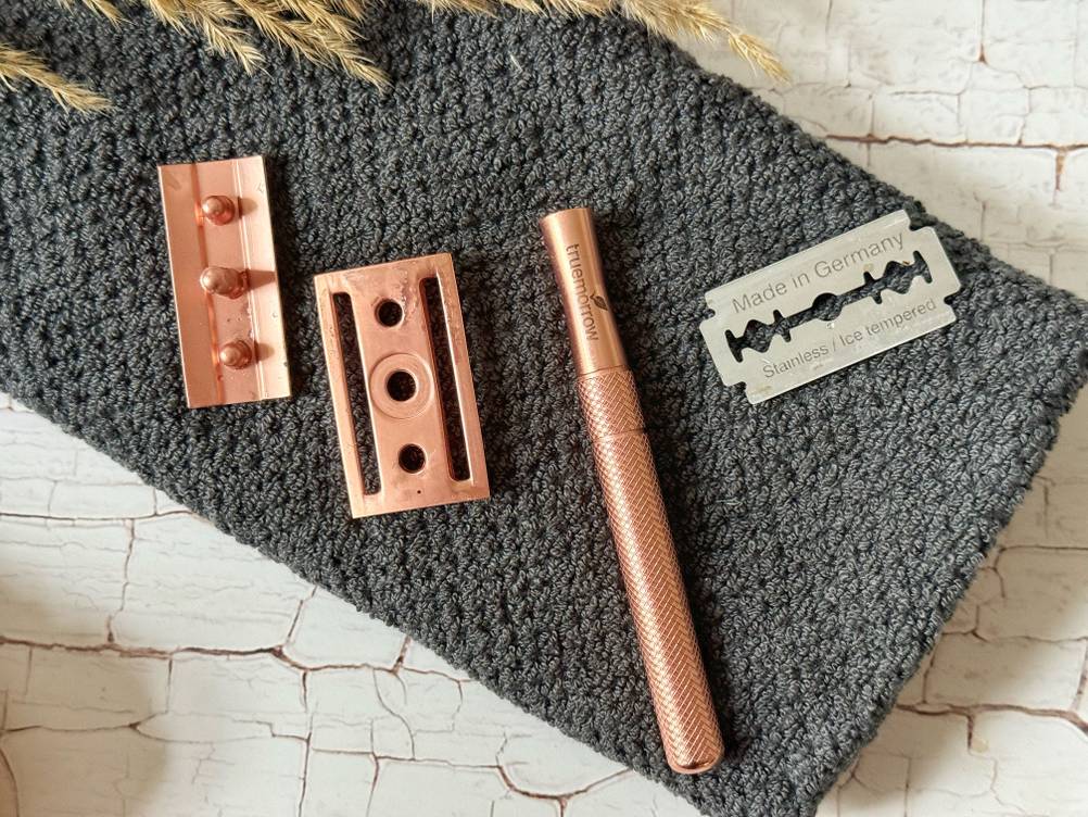 Rasierhobels für Frauen im Test: Einzelteile, inklusive Made in Germany-Edelstahl-Klinge, von einem rosé goldenen Metall-Rasierhobel der Marke Truemorrow liegen auf einem grauen Handtuch.