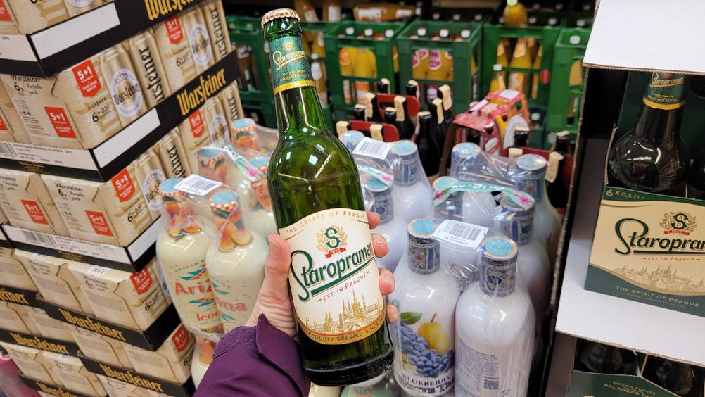 Eine Hand hält eine Flasche des Tschechischen Biers im Test hoch, im Hintergrund Getränkeflaschen.