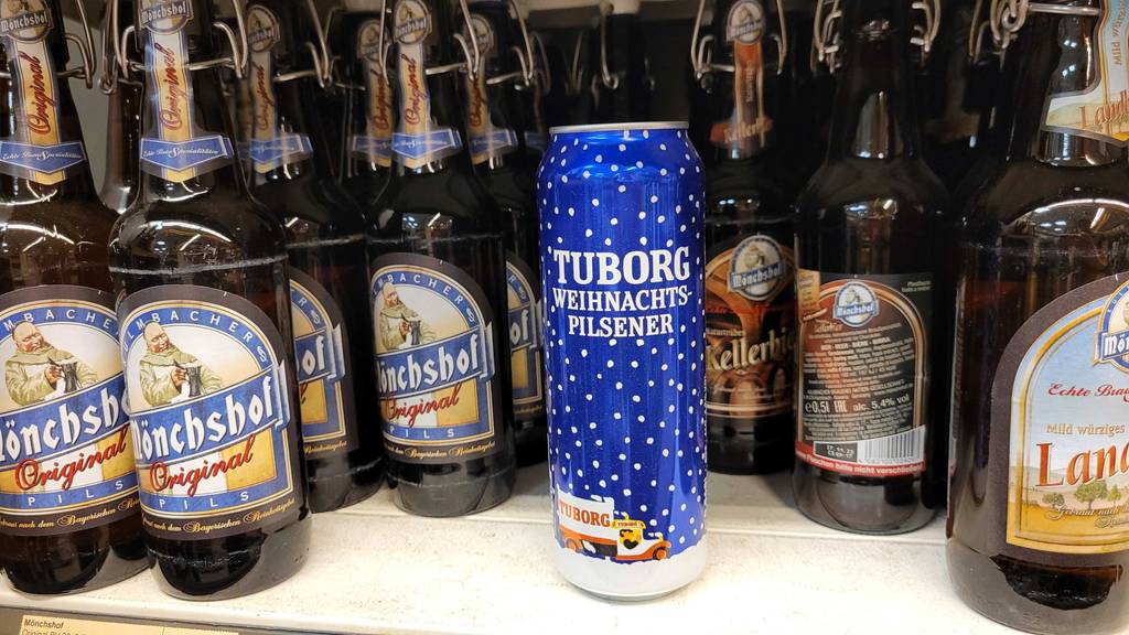 Getestet: Das Weihnachtsbier Pilsener im Weihnachtsdesign steht zwischen Bierflaschen auf einem Regal im Supermarkt.