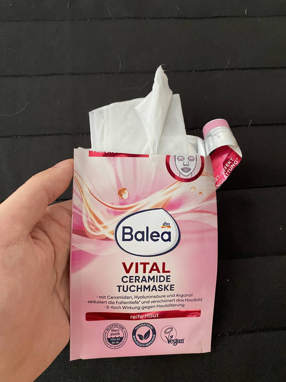 Eine Hand hält eine aufgerissene Packung der Tuchmaske im Test vor eine dunkle Fläche.