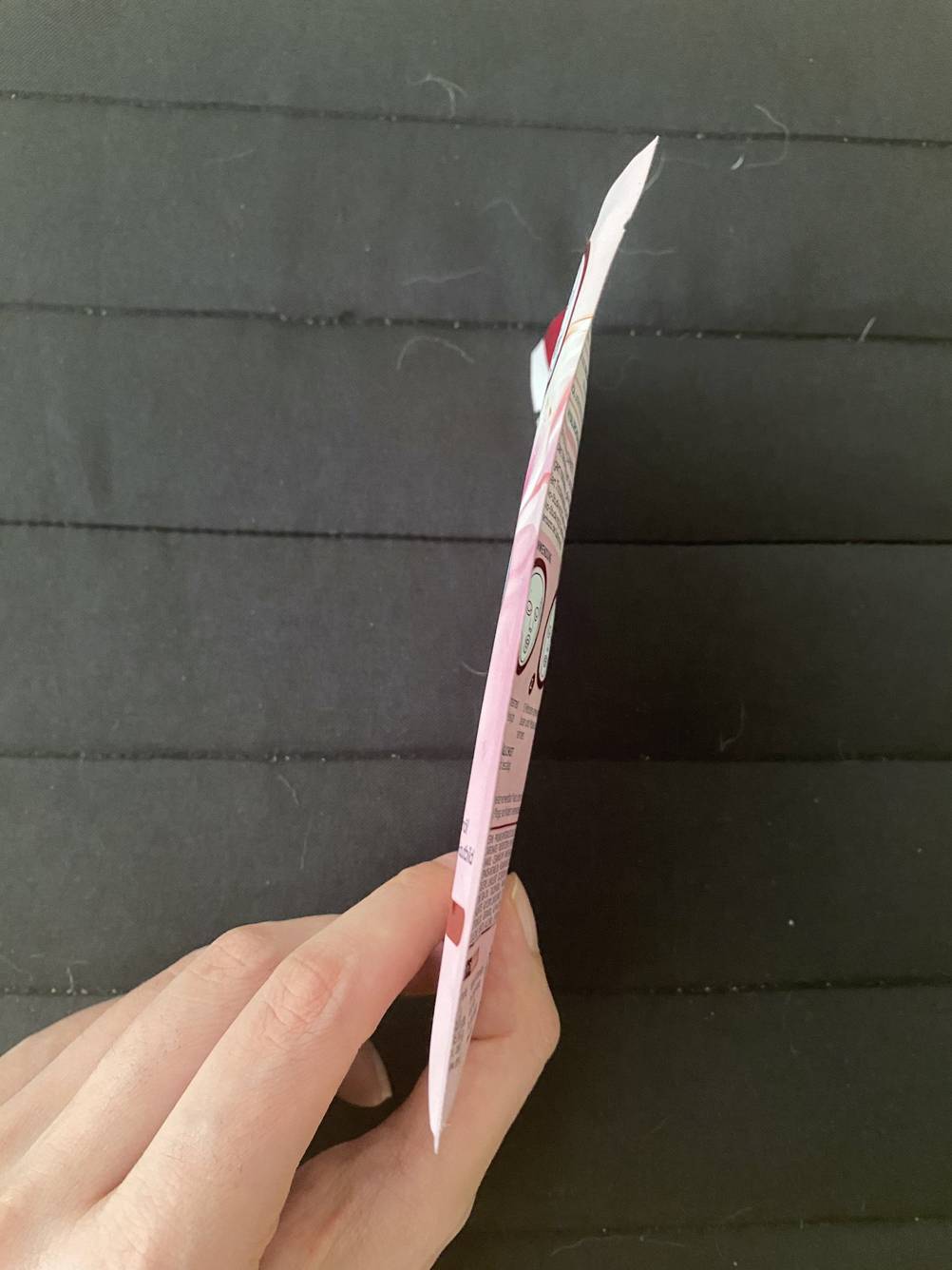 Tuchmaske-Test: Eine Hand hält die Packung seitlich vor eine dunkle Fläche.