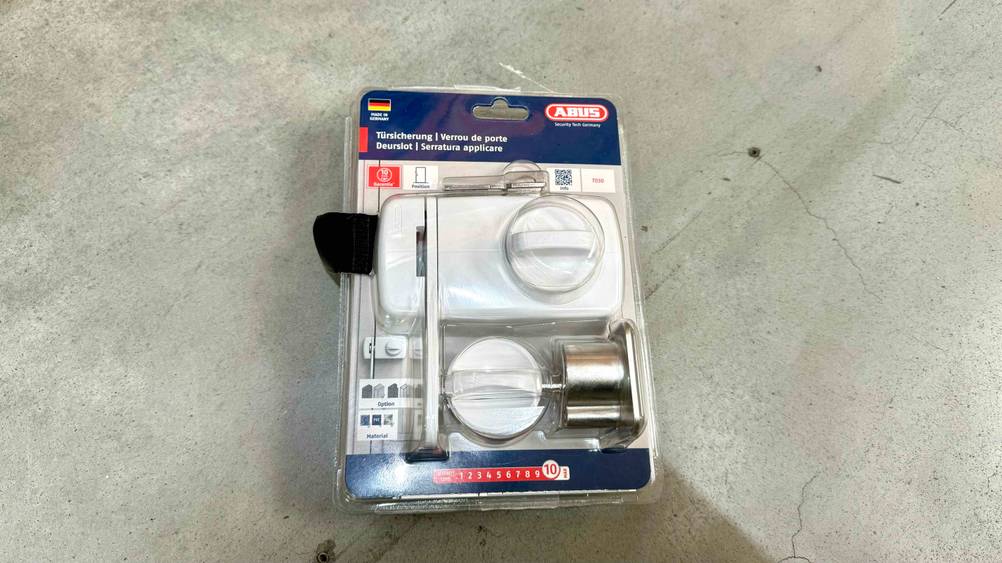 Tür-Zusatzschloss getestet: Ein transparent verpacktes Gerät auf einem Betonboden liegend.