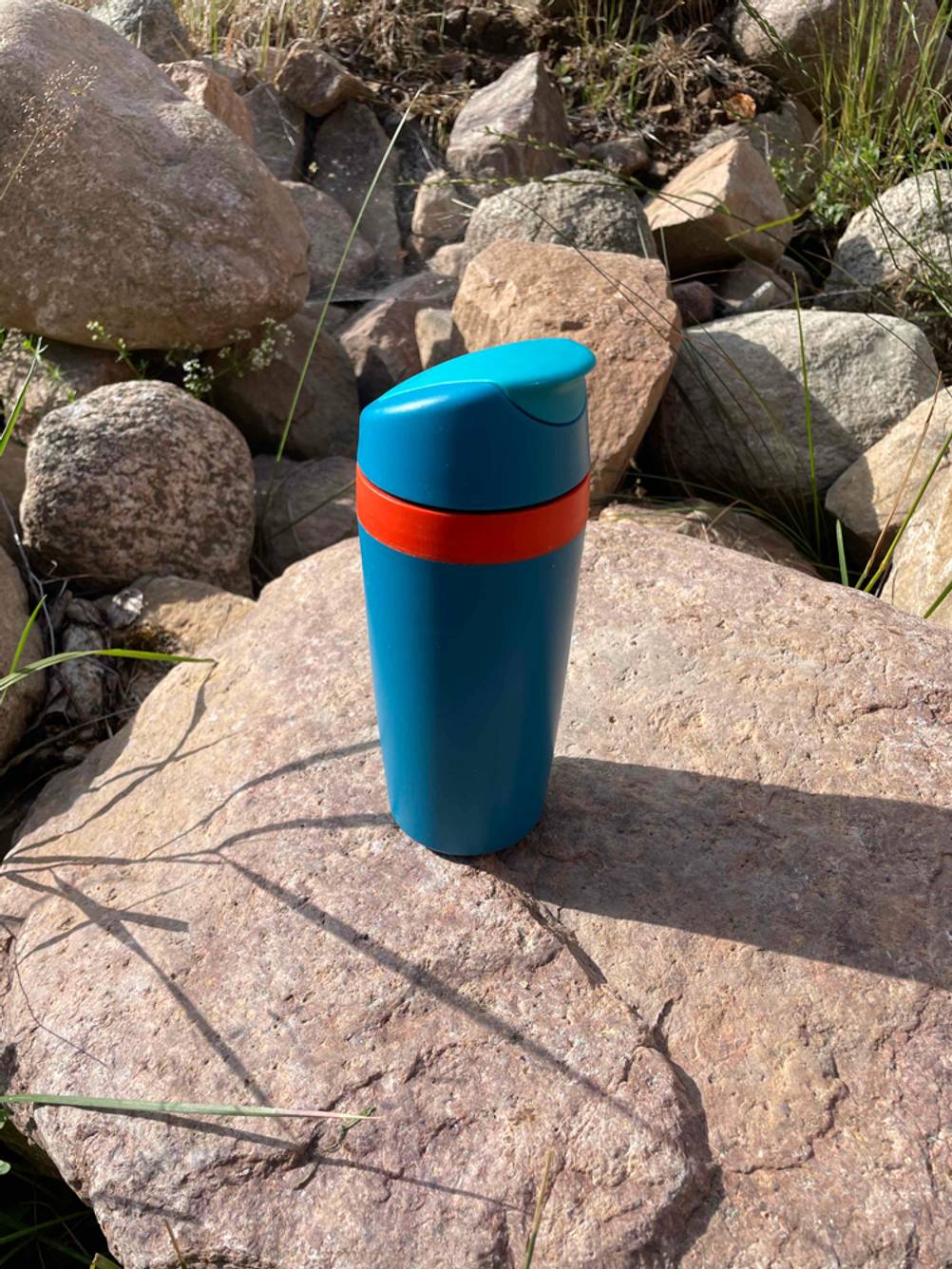 Im Test: Verschlossener Coffee-to-go Becher der Marke Tupperware steht auf einem Stein in Landschaft