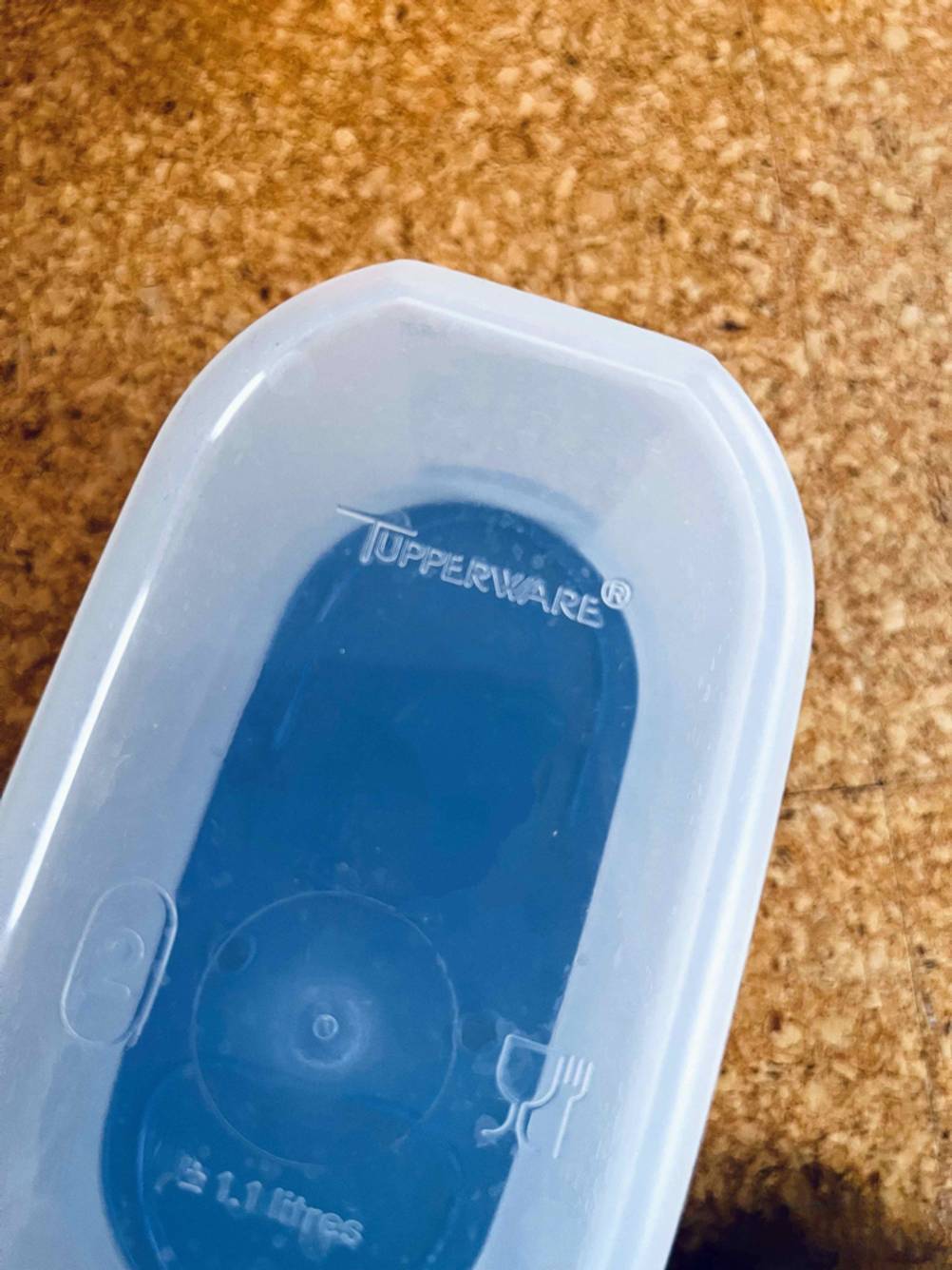 Tupperware-Test: transparenter Behälter mit blauem Deckel von unten betrachtet auf Kork.