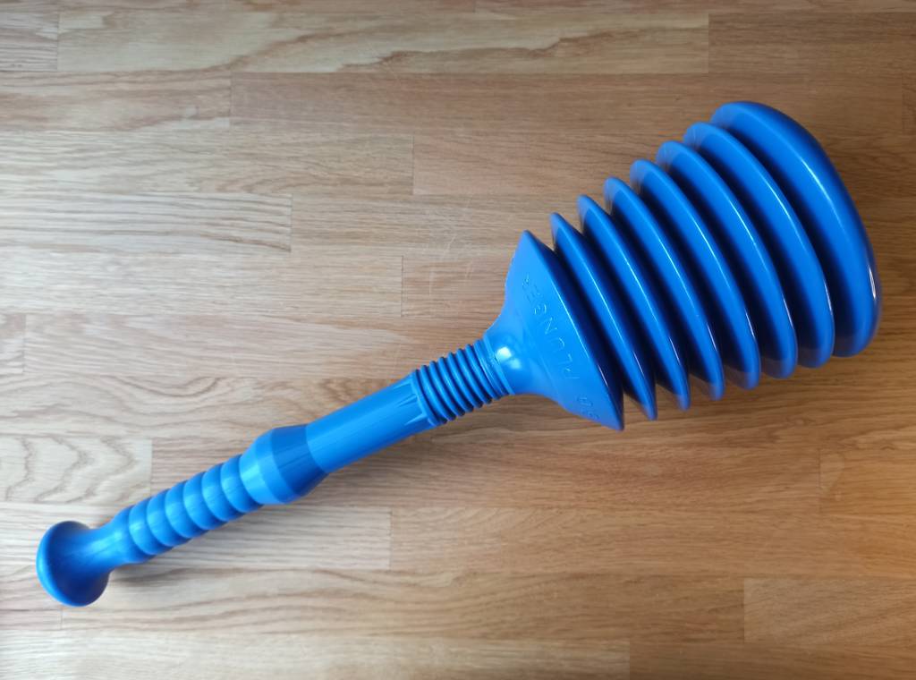 Ein Pömpel seitlich auf einer Holzoberfläche liegend.