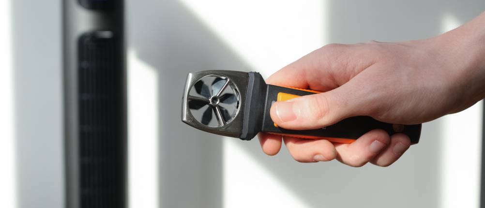 Mit einem Windmessgerät wird die Windstärke vor einem Turmventilator erfasst.