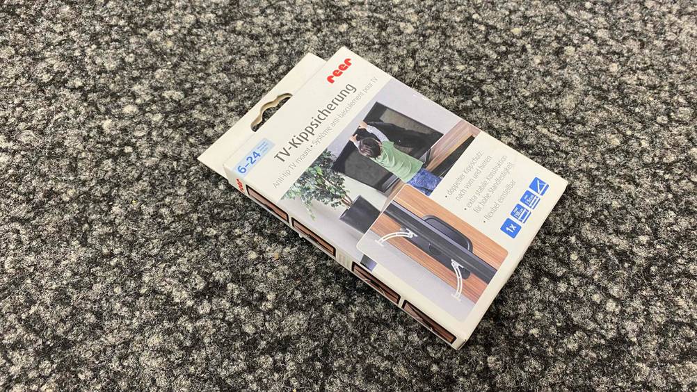 Auf dem Boden befindet sich eine getestete TV-Kippsicherung verpackt. 
