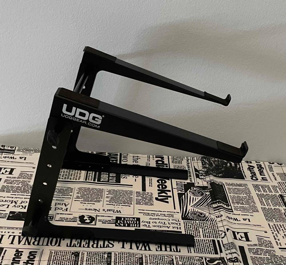 Ein getesteter Laptop-Ständer von UDG steht auf einem Tisch im Zeitungsdesign, von der Seite betrachtet.