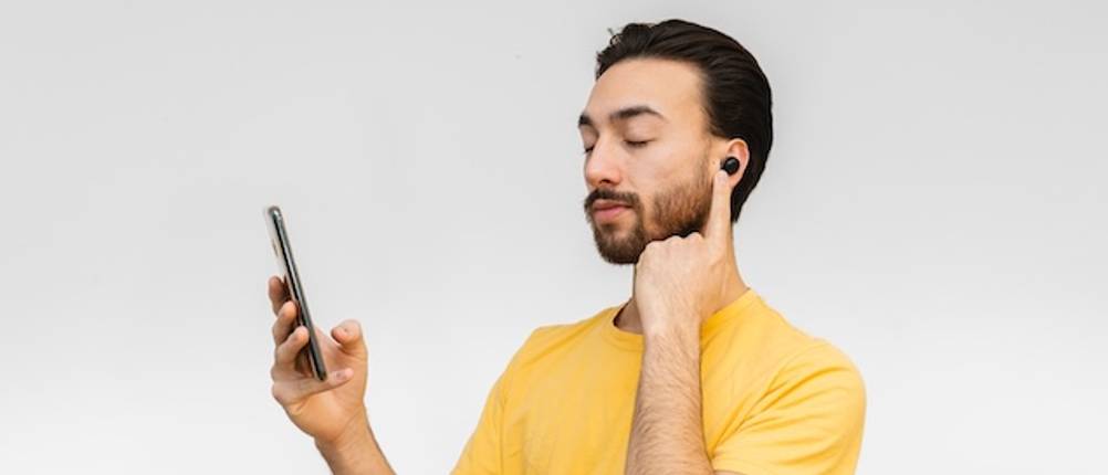 Übersetzungskopfhörer-Test: Ein Mann im gelben T-Shirt hat einen In-Ear-Kopfhörer eingesetzt und schaut auf sein Smartphone.