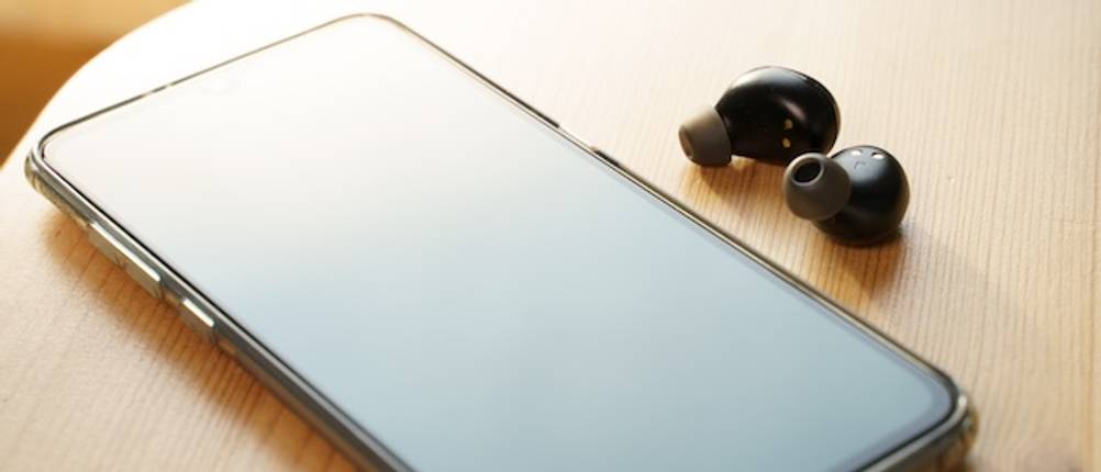 Getestete Übersetzungskopfhörer liegen auf einem hellen Holztisch neben einem Smartphone.