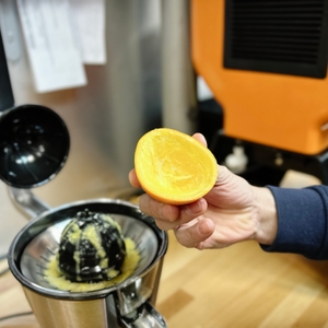 Eine Hand hält eine ausgepresste Orangenschale über der Ufesa Zitruspresse EX4950. Das Innere der Fruchthälfte ist vollständig leer.