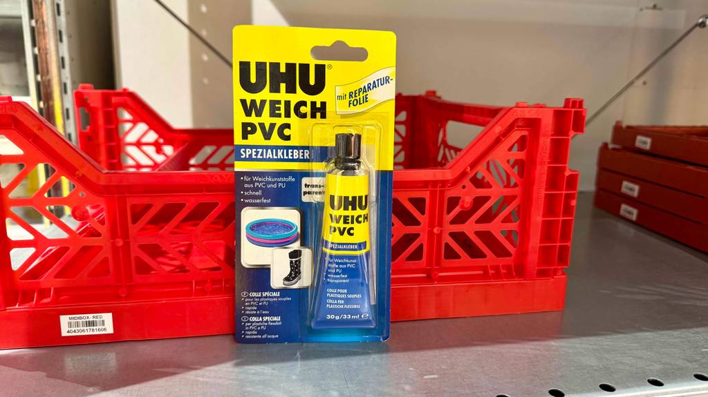 Eine Tube PVC-Kleber steht im Blister zum testen vor einer roten Plastikgitterbox.