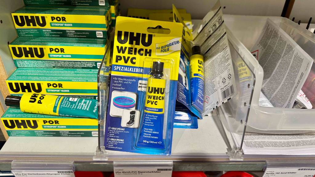 PVC-Kleber im Test: Mehrere verpackte Tuben liegen kreuz und quer zwischen anderen Produkten in einem Regal.