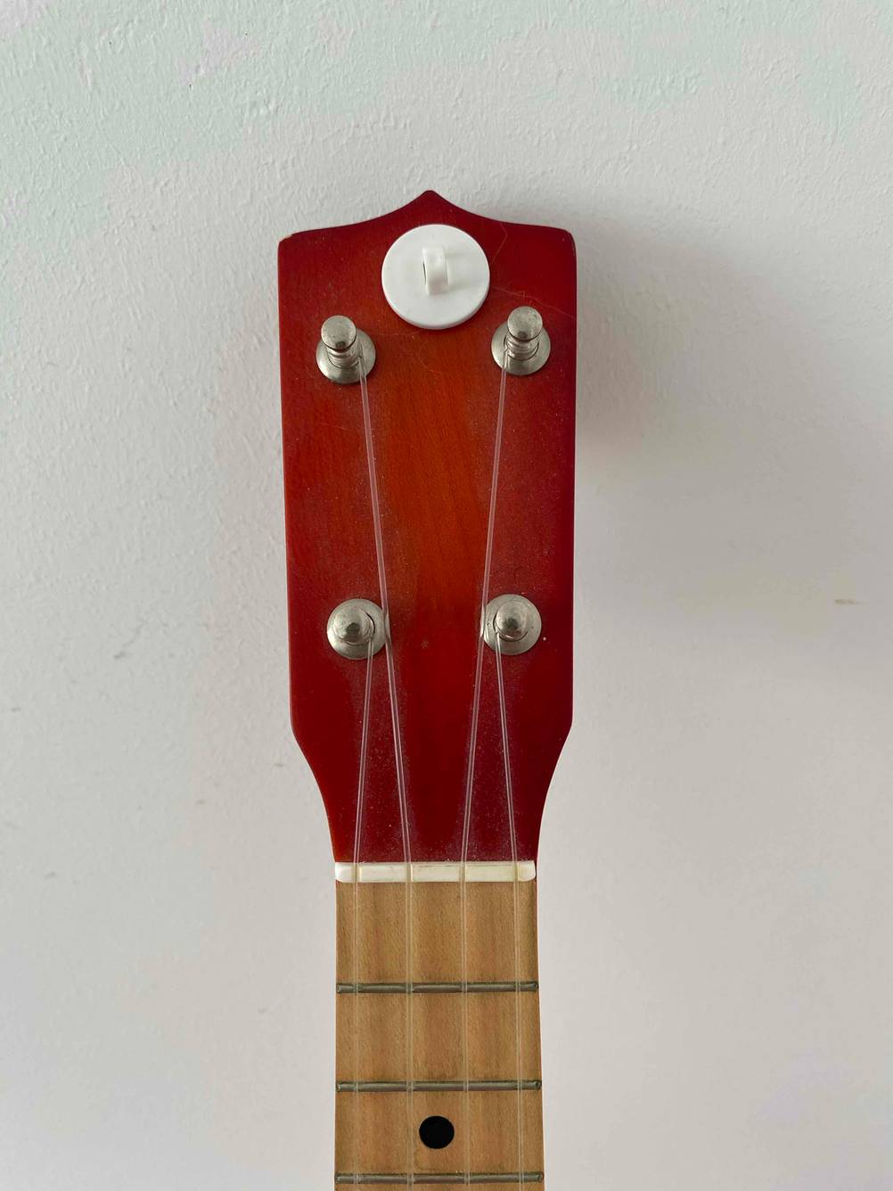 Nahaufnahme der Kopfplatte einer Ukulele im Test an einer hellen Wand.