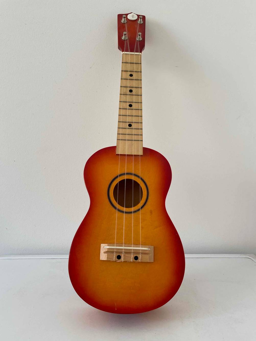 Eine getestete Ukulele von vorne an einer Wand lehnend.