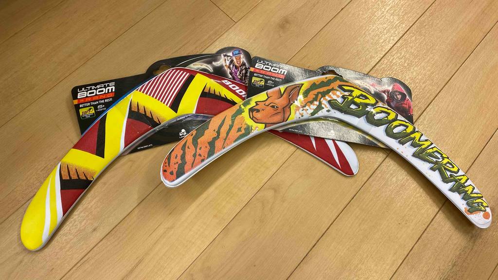 Zwei verpackte Boomerangs liegen zum Test übereinander auf einem hellen Holzboden.