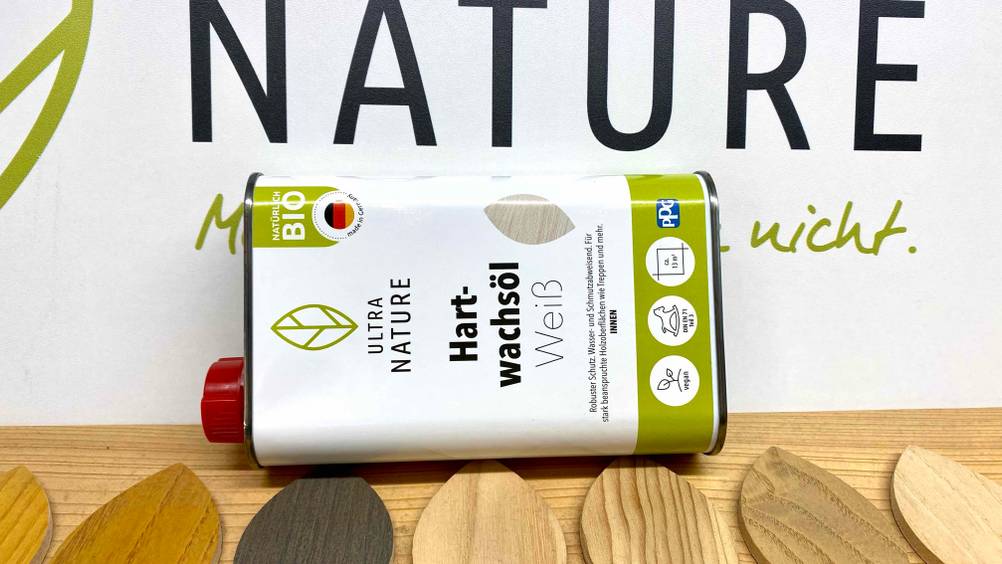 Eine Dose Hartwachsöl zum testen liegt quer vor einem großen Werbeplakat mit Nature Aufdruck.