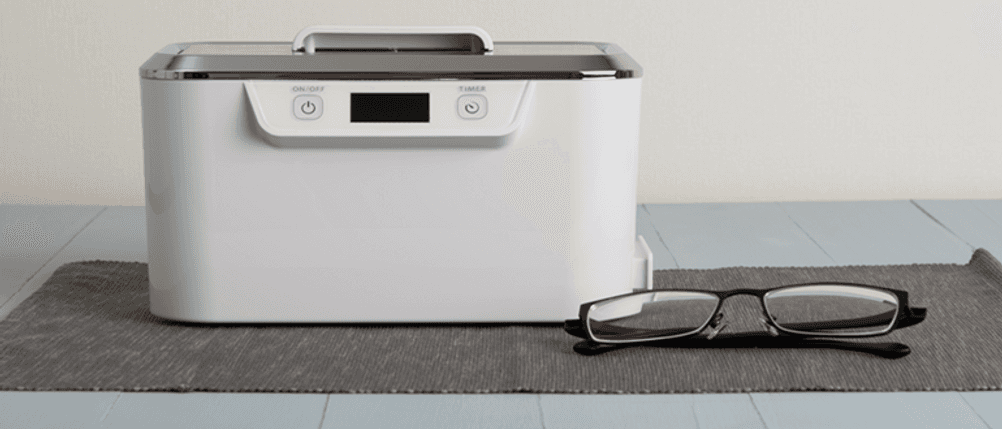 Ultraschallreiniger für Zahnprothese im Test: Eine Brille liegt neben einem Ultraschallgerät.