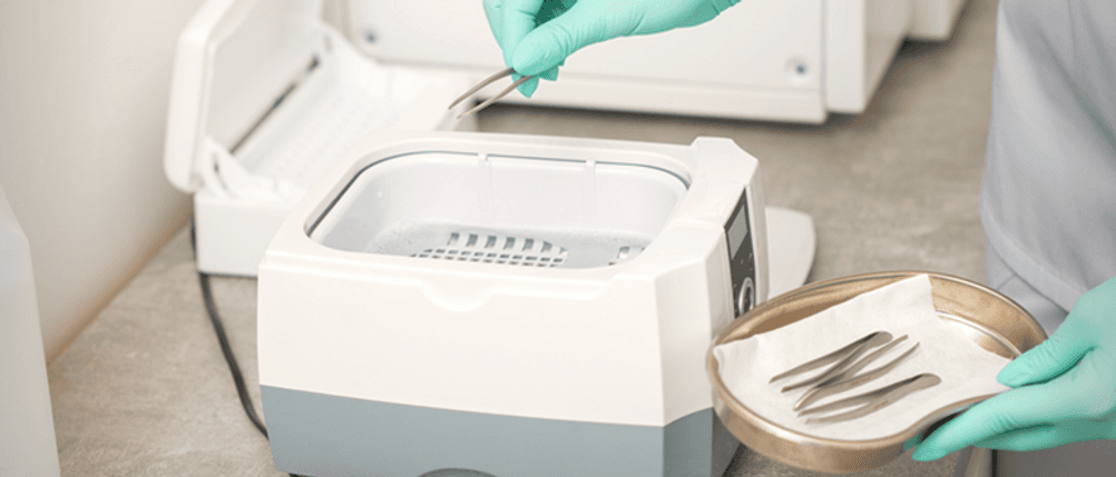 Ultraschallreiniger für Zahnprothese im Test: Eine Person legt eine Pinzette in ein Ultraschallbad.