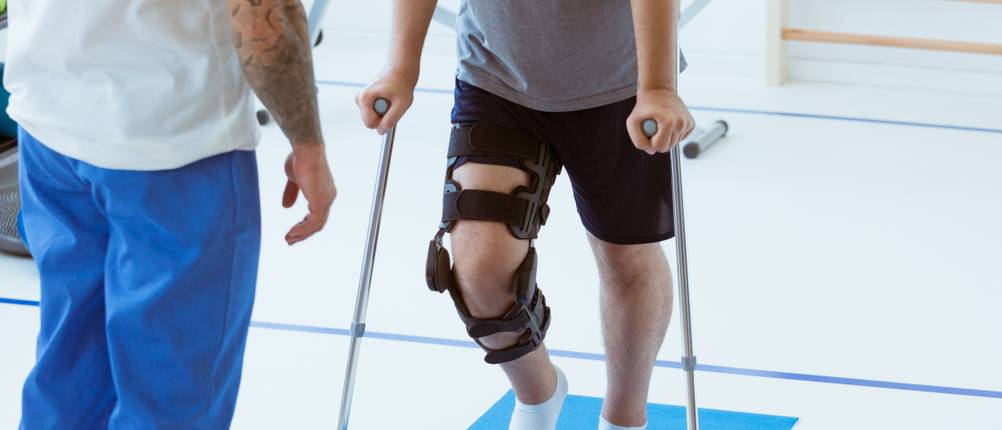Unfallversicherung-Test: Ein Mann hat eine Schiene am Knie und geht auf Krücken.