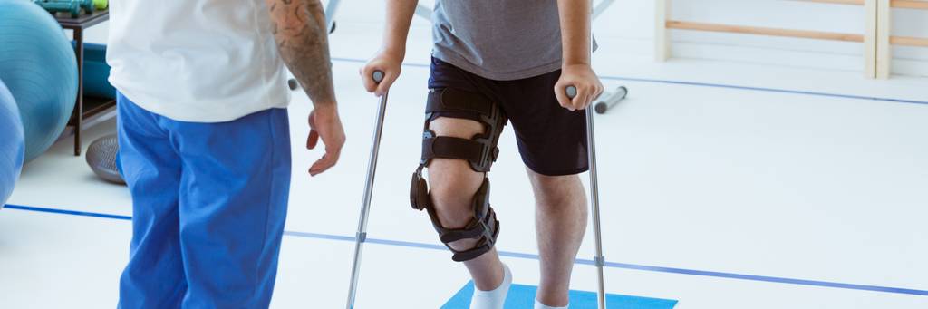 Ein Mann hat eine Schiene am Knie und geht auf Krücken.