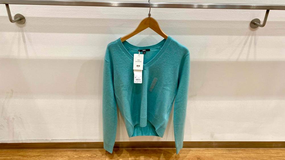 An einem Handlauf häng auf einem Bügel ein Kaschmir-Pullover für Damen im Test vor einer hellen Wand.