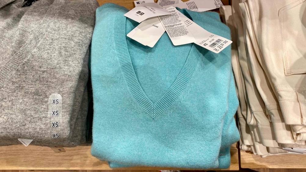 Kaschmir-Pullover für Damen-Test: Ein gefalteter Kaschmir-Pullover liegt neben anderen Kleidungsstücken in einer Verkaufsfläche.