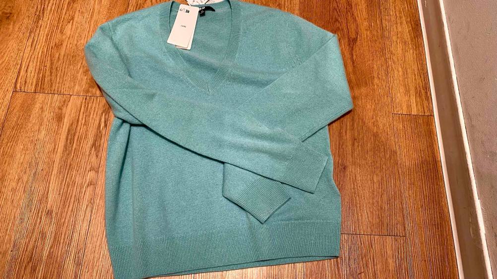 Kaschmir-Pullover für Damen getestet: Ein Pullover liegt mit vorne gefalteten Ärmeln auf einem Holzboden.