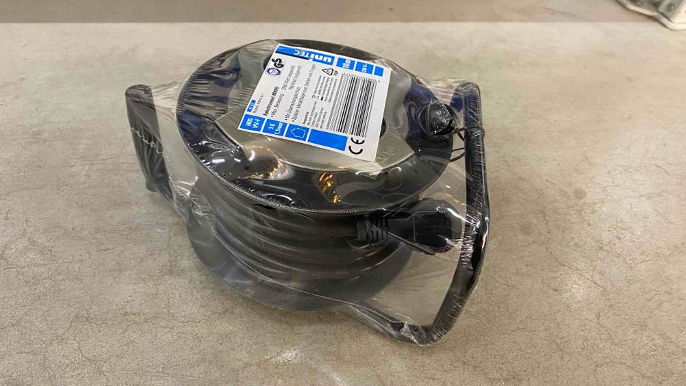 Kabeltrommel getestet: Eine transparent verpackte Trommel auf der Seite liegend auf einem Betonboden.