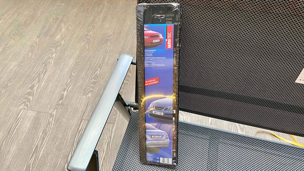 Ein verpackter Kennzeichenhalter steht hochkant zum testen auf einem Stuhl.