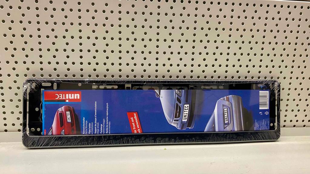 Im Test: Ein verpackter Kennzeichenhalter lehnt an eine Lochwand.