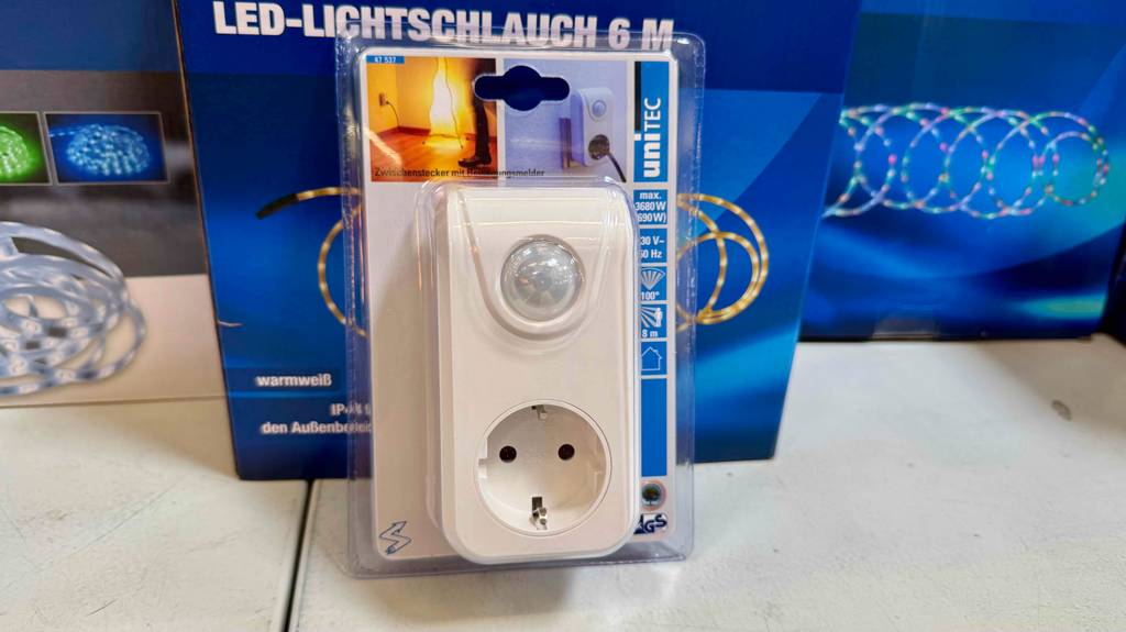 Im Test: Das Nachtlicht mit Bewegungsmelder und Steckdose befindet sich eingeschweißt in der transparenten Kunststoffverpackung vor Kartons mit Lichterketten.