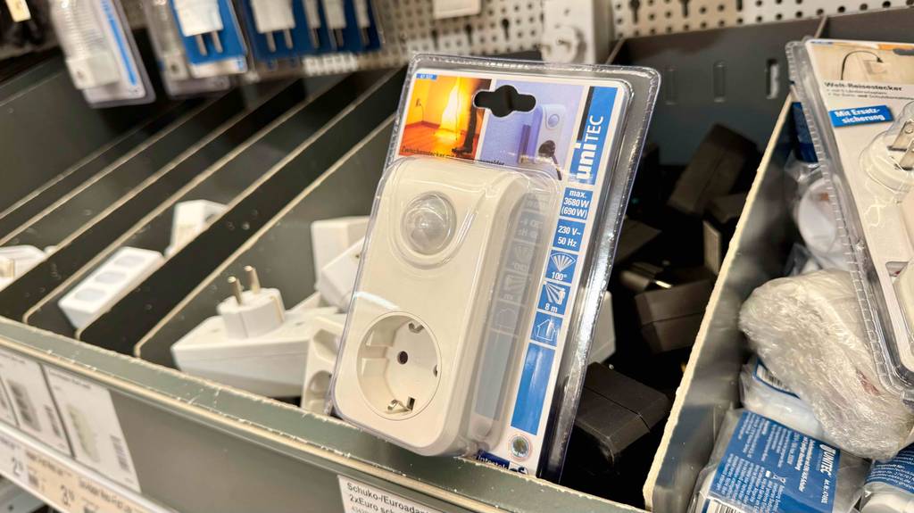 Das getestete Nachtlicht mit Bewegungsmelder und Steckdose liegt innerhalb der transparenten Kunststoffverpackung auf einem Regal mit weiteren Steckermodellen.