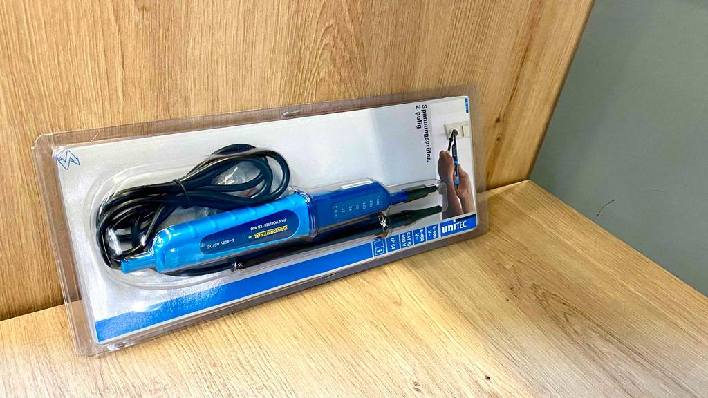 Ein elektrischer, blauer Unitec Spannungsprüfer im Test liegt in seiner Originalverpackung auf einer Holzfläche.