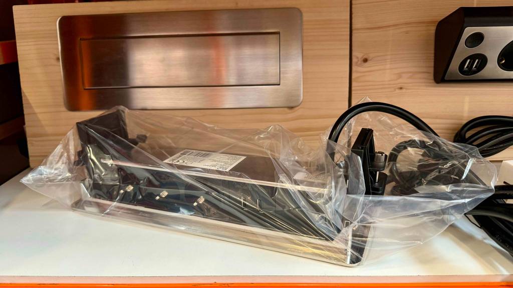 Versenkbare Steckdose im Test: Ein in Folie verpacktes Gerät liegt mit der Rückseite nach oben vor einem geschlossenen eingebauten.