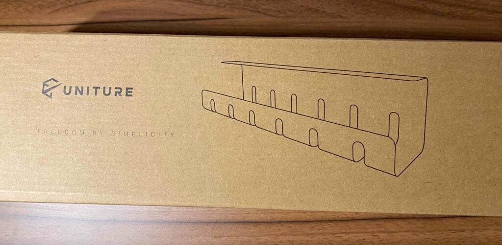 Ein brauner Uniture Verpackungskarton eines getesteten Kabelkanals liegt auf einer Holzoberfläche.