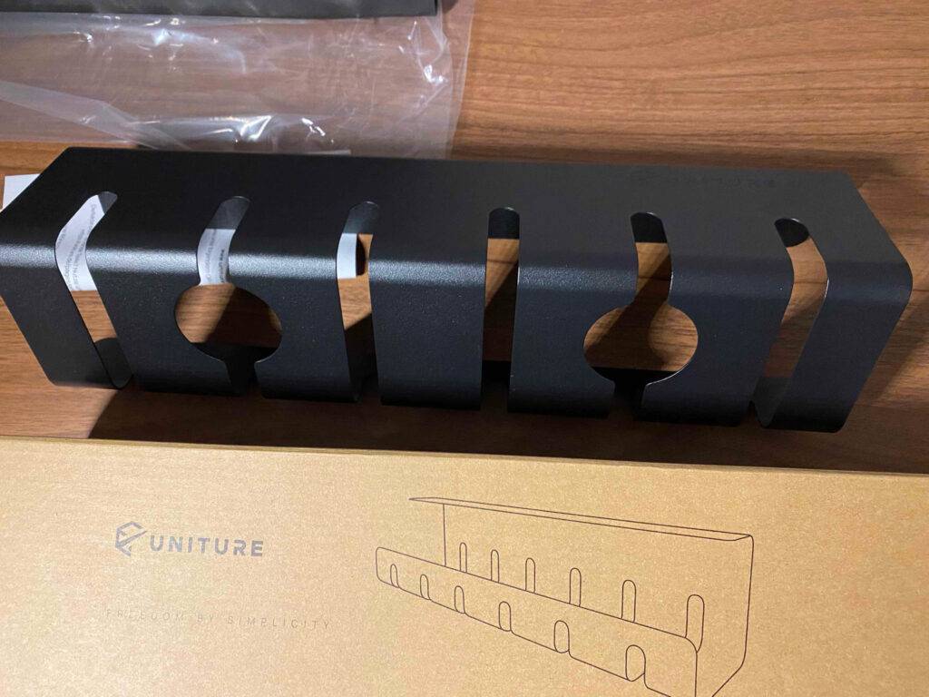 Kabelkanal-Test: Ein schwarzes Metall-Modell der Marke Uniture liegt oberhalb seines braunen Verpackungskartons.