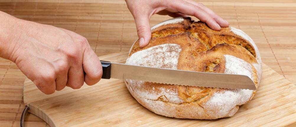 Universalmesser im Test: Brot liegt auf Holzbrett und wird mit Brotmesser geschnitten.