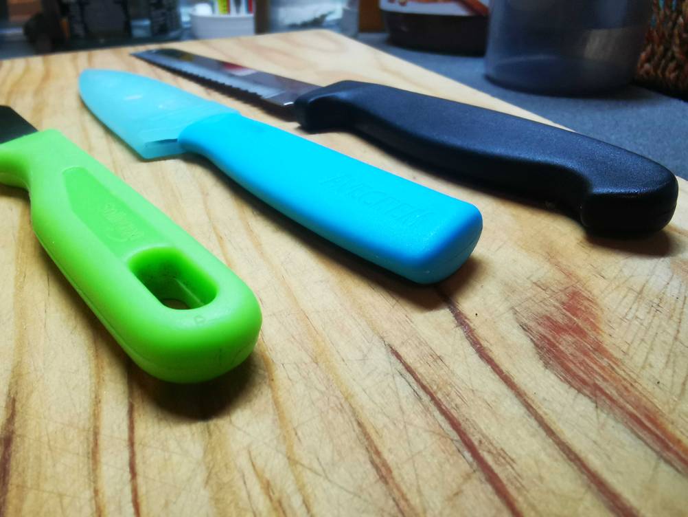 Nahaufnahme der Griffe dreier Universalmesser im Test auf einer Holzfläche.