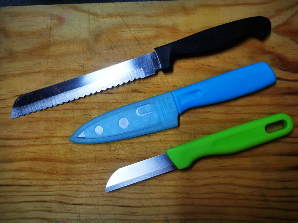 Drei unterschiedliche Universalmesser im Test nebeneinander auf einer Holzfläche.