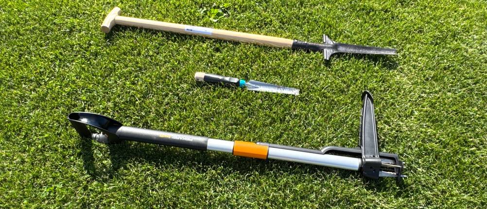 Drei Unkrautstecher liegen nebeneinander auf Gras.