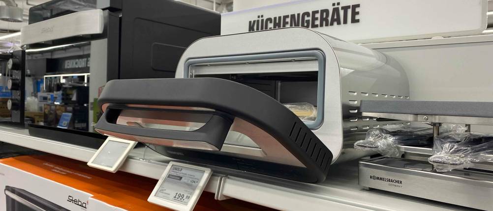 Im Test: Ein Pizzaofen (elektrisch) mit geöffneter Klappe und Preisschild auf einem Verkaufsregal.