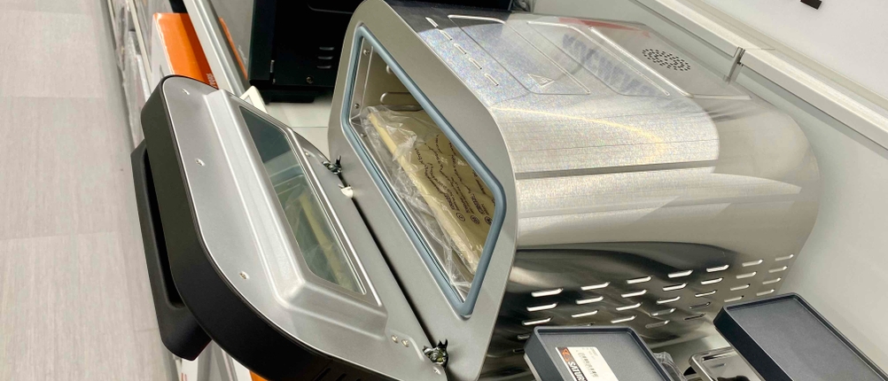 Ein Pizzaofen (elektrisch) im Test von schärg oben mit geöffneter Klappe zwischen anderen Geräten auf einem Regal.