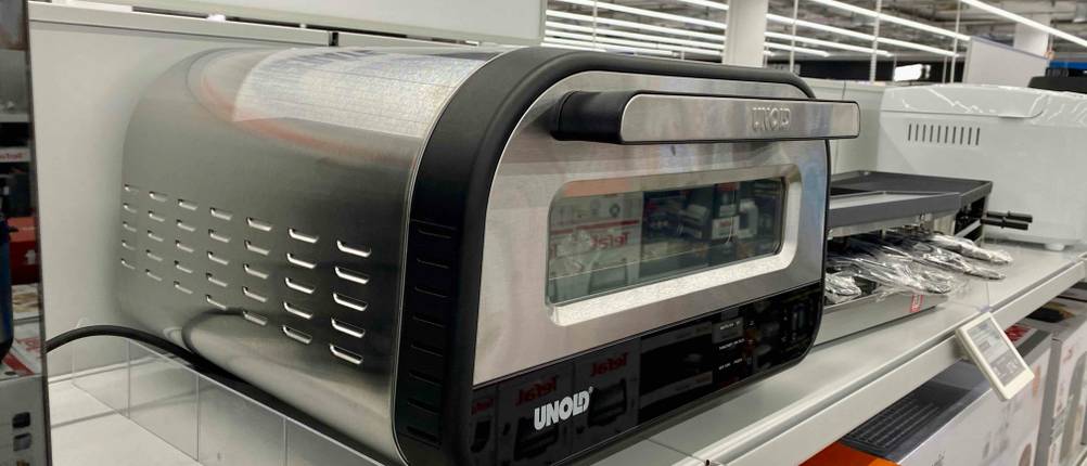 Ein getesteter Pizzaofen (elektrisch) auf einem Verkaufsregal von schräg seitlich mit geschlossener Klappe.